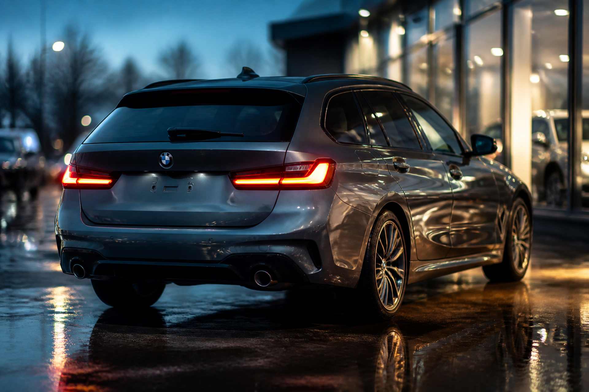 Retro tre quarti della BMW 318d Touring con fanali LED accesi sul piazzale bagnato