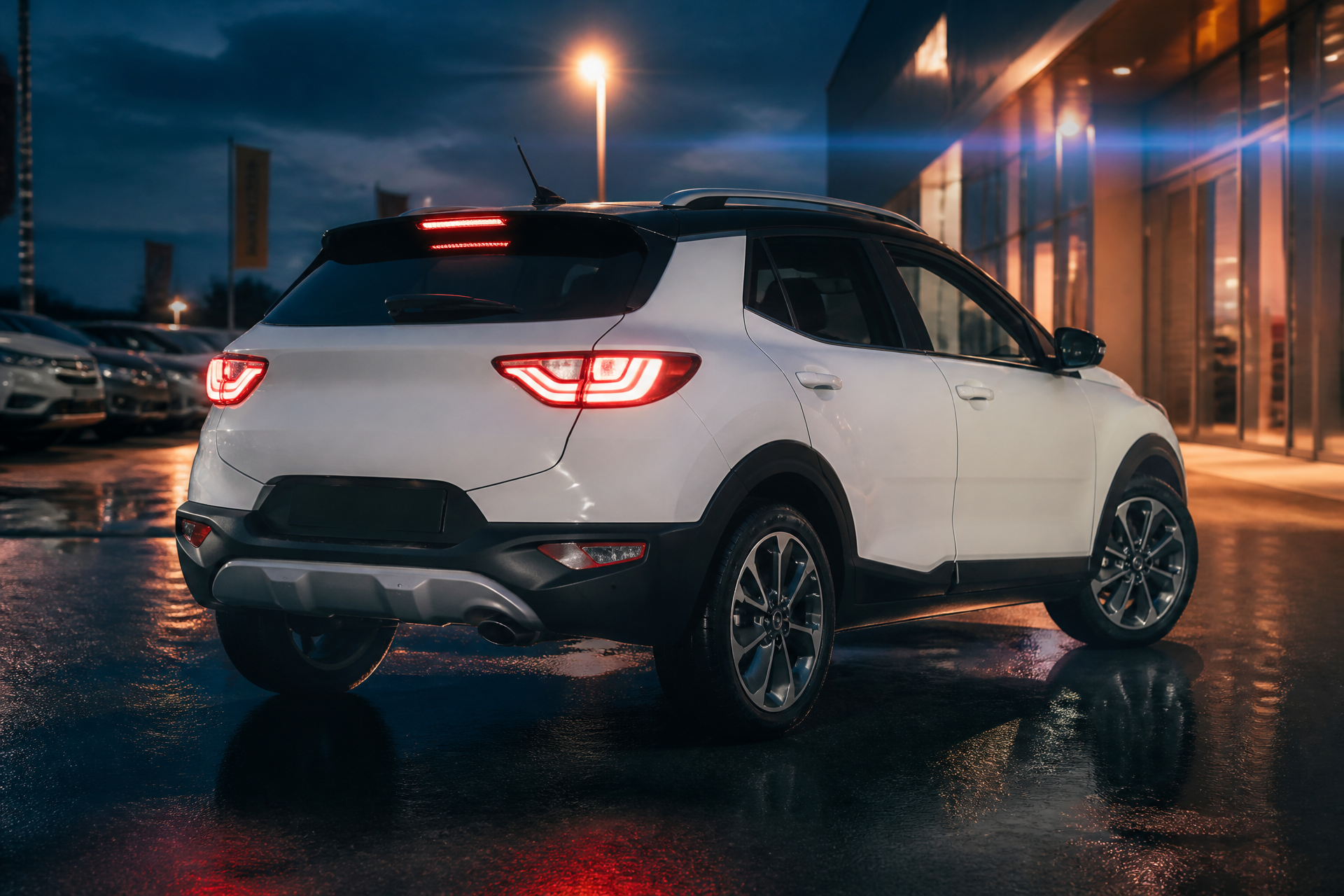 Retro tre quarti della Kia Stonic con fanali accesi e riflessi sul piazzale bagnato