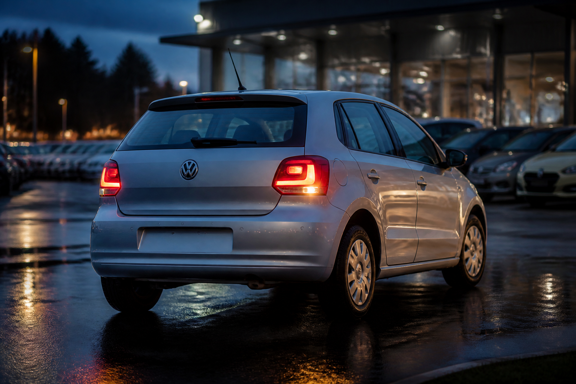Retro tre quarti della Volkswagen Polo con fanali accesi in serata sul piazzale AutoConte